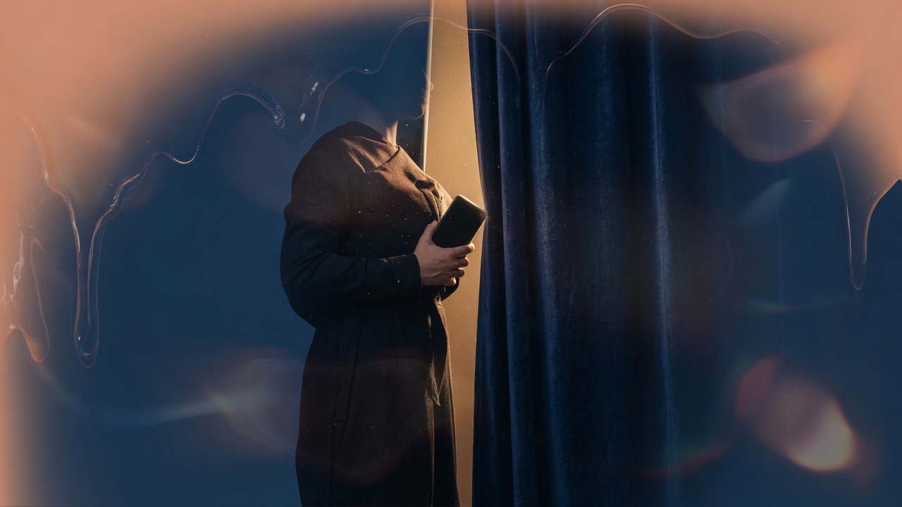 An adult holding a phone against their chest beside a heavy curtain